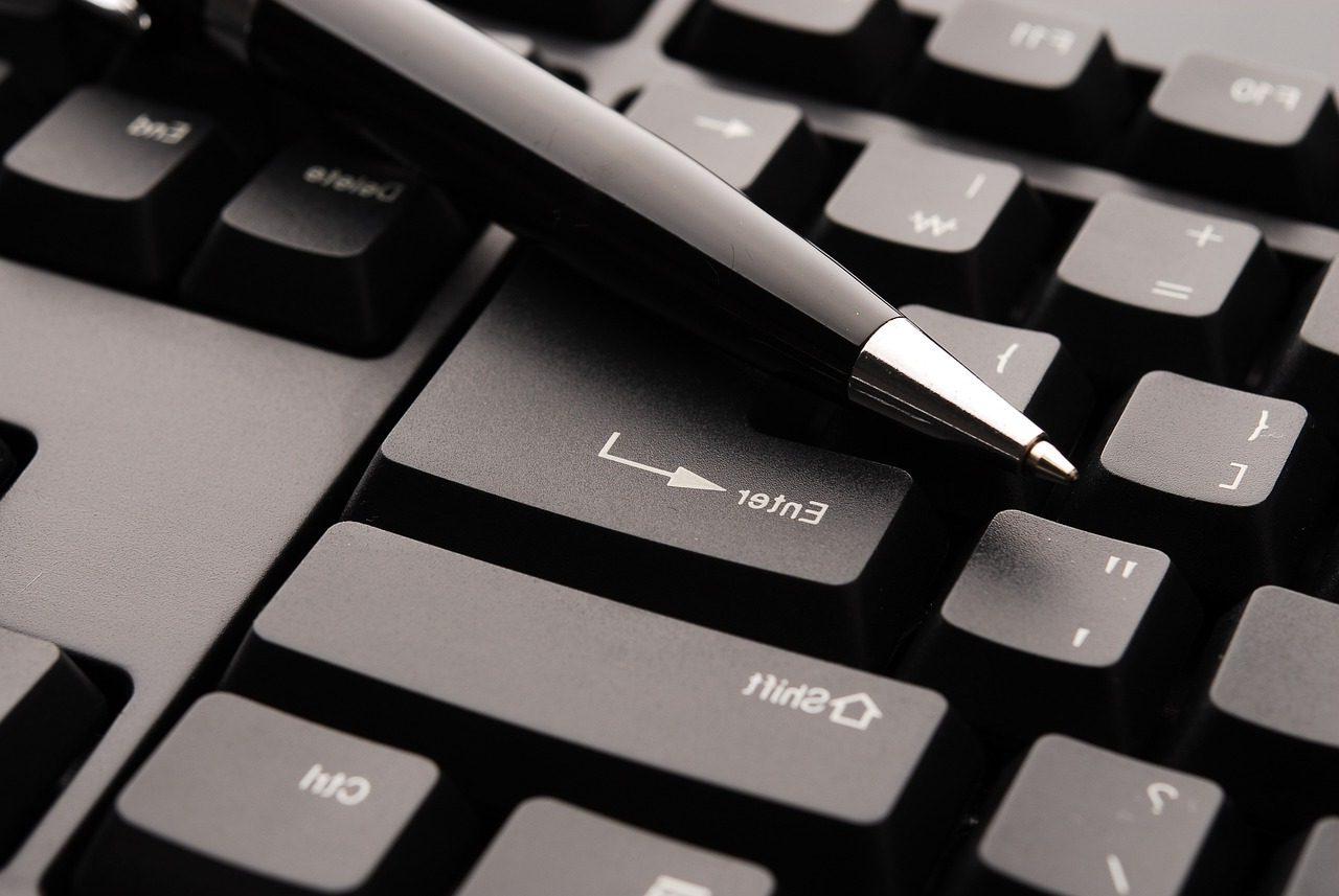 Close-up image of a black pen laid on top of a black keyboard.